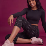 Woman in black crop top and polka dot leggings with pink sneakers on a magenta background